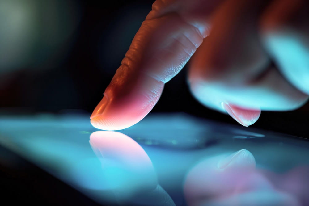 Détail d'un index touchant la surface lumineuse d'un tactile écran avec des reflets bleutés