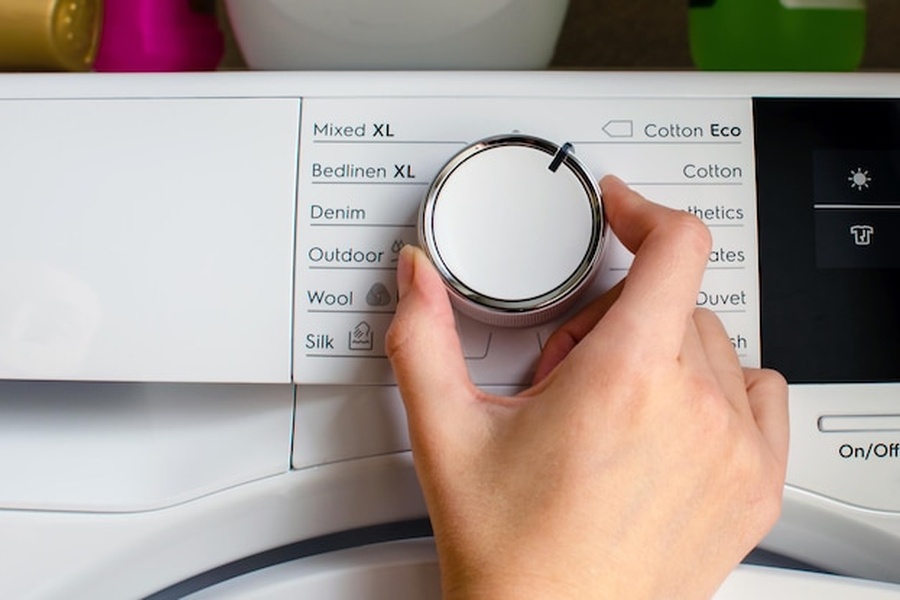 Main réglant le sélecteur de programmes d'un lave-linge dont l'indice de réparabilité favorise un entretien durable.
