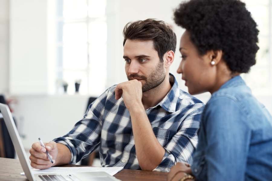 Un homme et une femme travaillent ensemble sur un ordinateur portable dans un bureau lumineux.