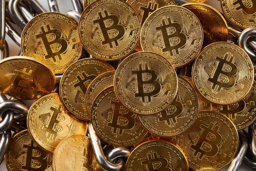 Un amas dense de pièces physiques de Bitcoin dorées reposant sur une lourde chaîne en métal argenté.