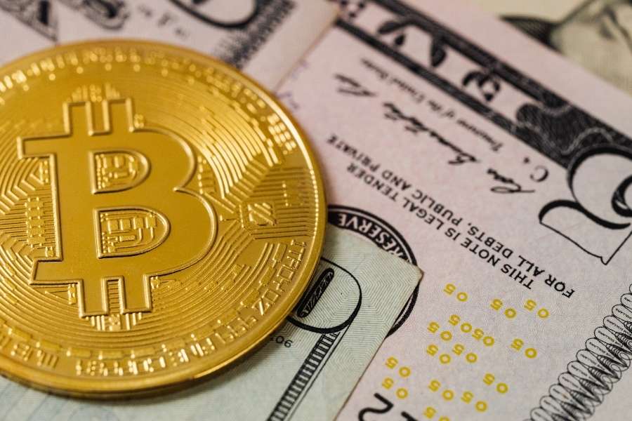 Une pièce dorée de Bitcoin posée sur des billets de banque pour illustrer l'impact des tendances macroéconomiques.