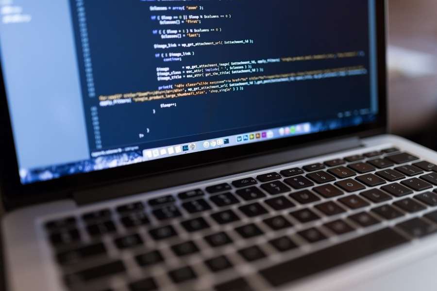 Un écran d'ordinateur portable affiche des lignes de code informatique, illustrant l'analyse technique pour la veille concurrentielle de son site web.